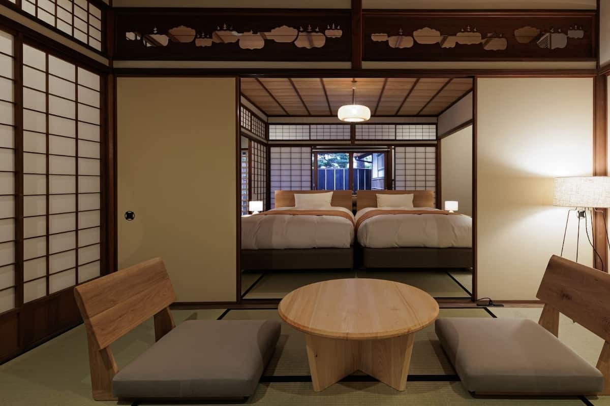 Ett traditionellt japanskt rum med tatamimattor på golvet, ett runt träbord, två låga trästolar och en säng med en futonmadrass.