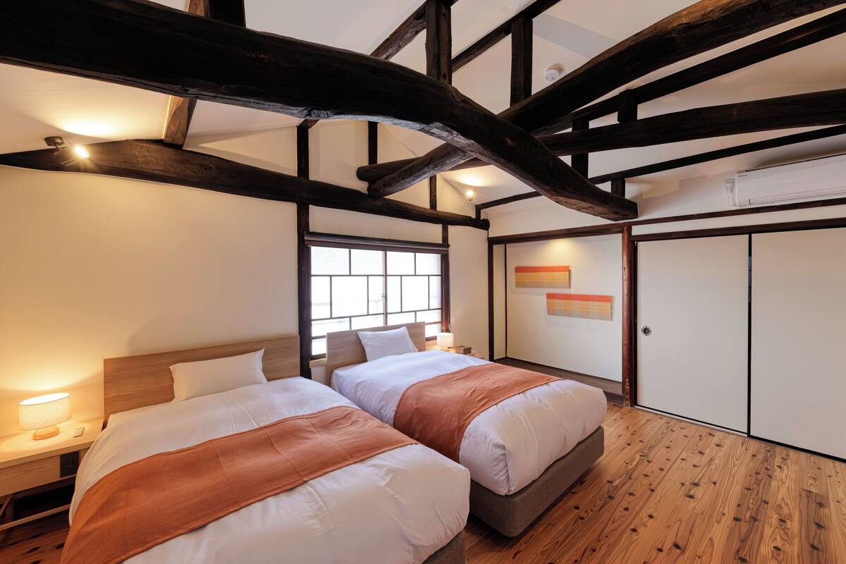 Une chambre avec deux lits, des poutres en bois, une fenêtre et une armoire.