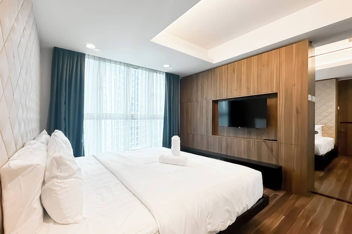 Una habitación de hotel moderna con una cama grande, un televisor de pantalla plana montado en la pared y vistas de la ciudad a través de amplios ventanales.