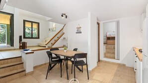 A modern kitchen with a dining area, wooden staircase, and a view of the outdoors.