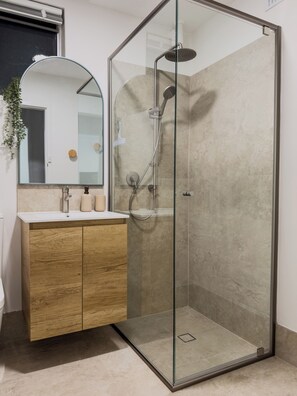 Un baño moderno con ducha acristalada, tocador de madera y un espejo grande.