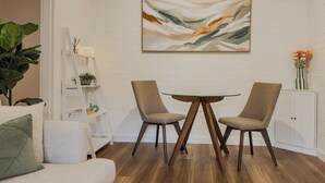 A modern living room with a white sofa, a glass-top coffee table, two armchairs, a white bookshelf, and a painting on the wall.