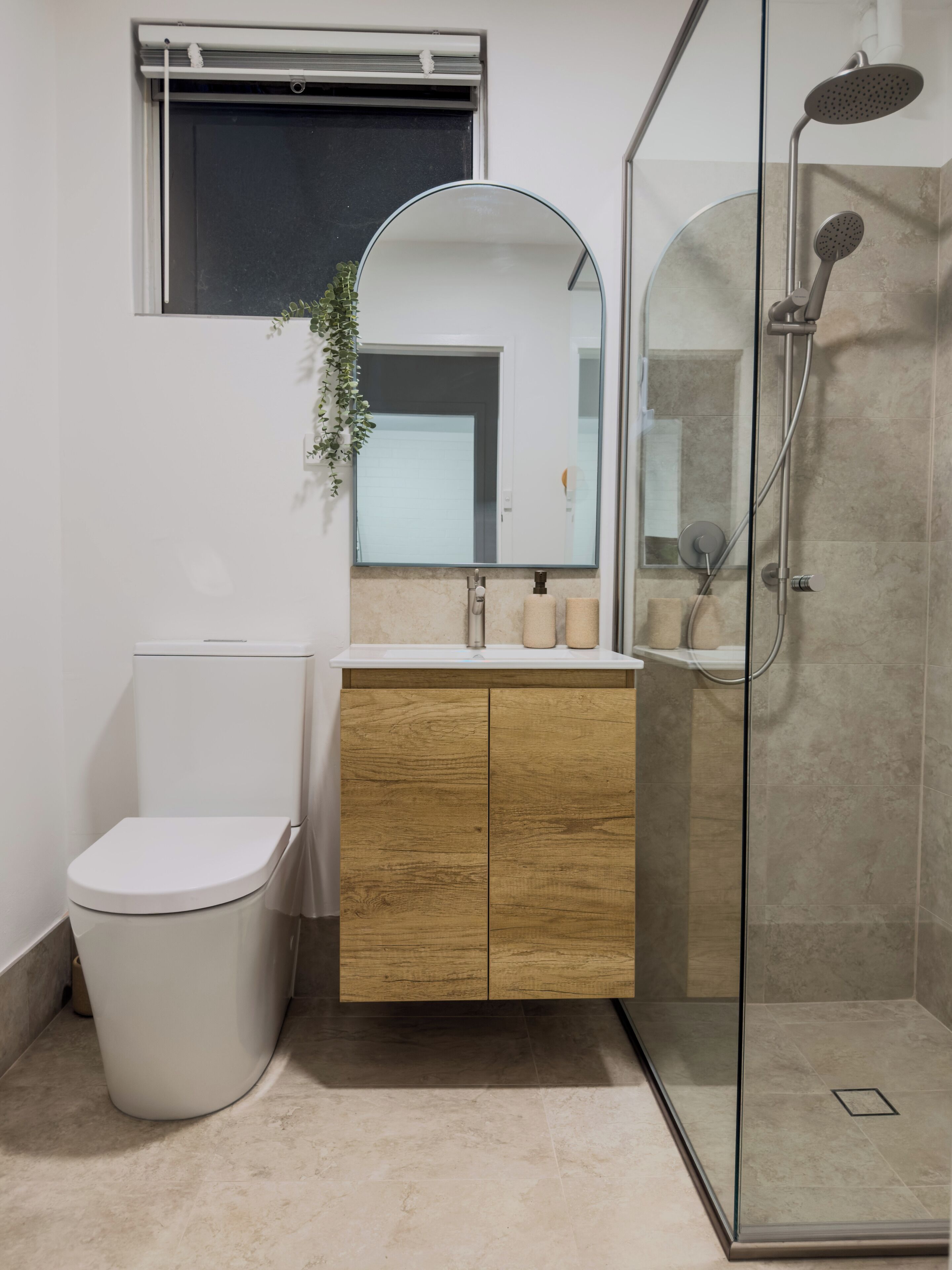 A modern bathroom with a toilet, wooden vanity, mirror, and glass shower enclosure.