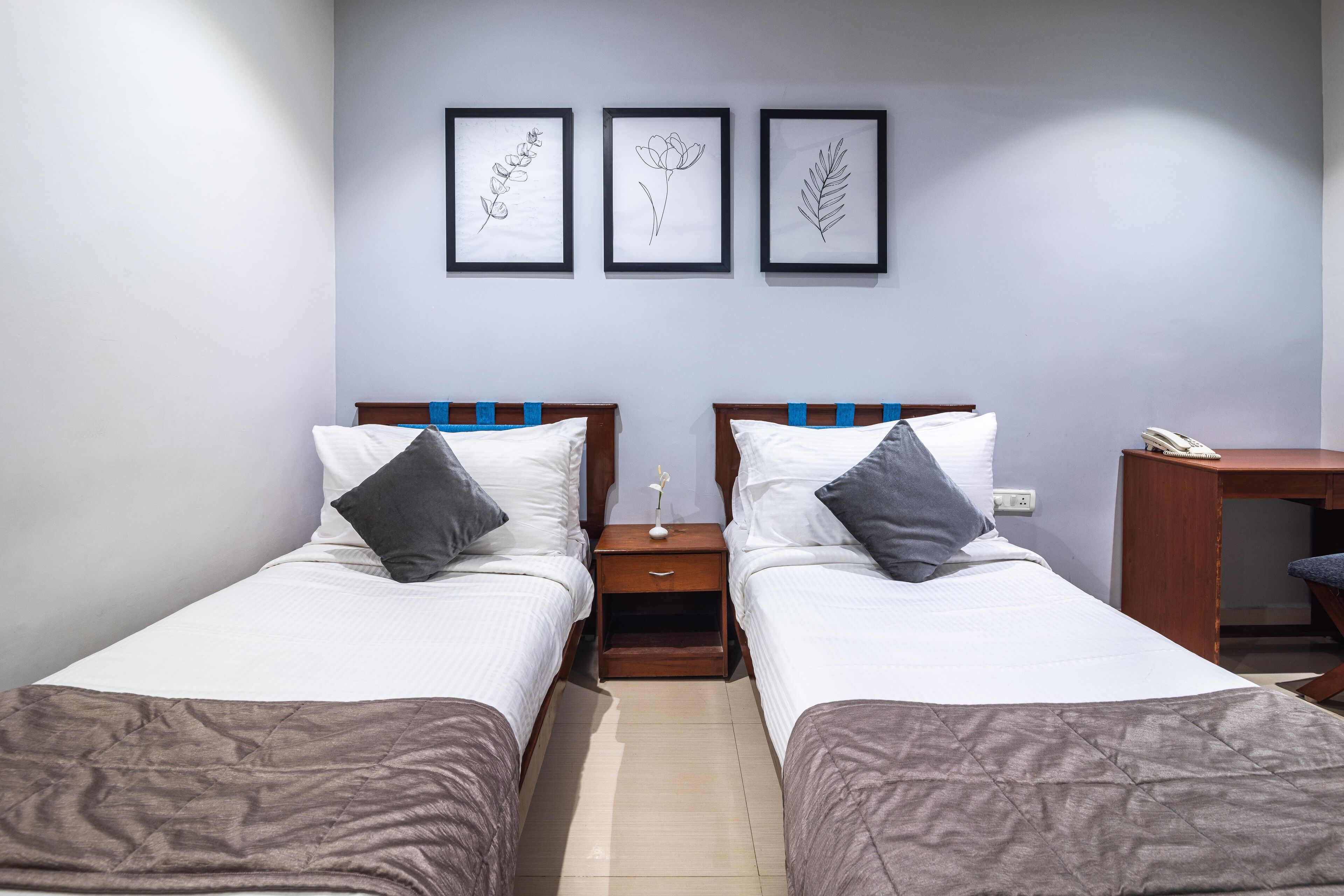 Quarto duplo com duas camas, mesa de cabeceira e escrivaninha. Quadros botânicos emoldurados adornam a parede.