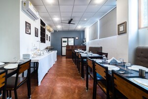 Un comedor con mesas largas dispuestas para varias personas, sillas y una barra de buffet.