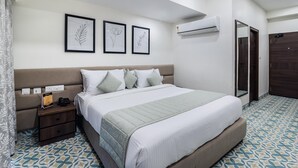 A neatly arranged bedroom with a bed, bedside tables, a nightstand, an air conditioning unit, and a door. - Ashreya Suites Tiruvanamalai (Tiruvannamalai)