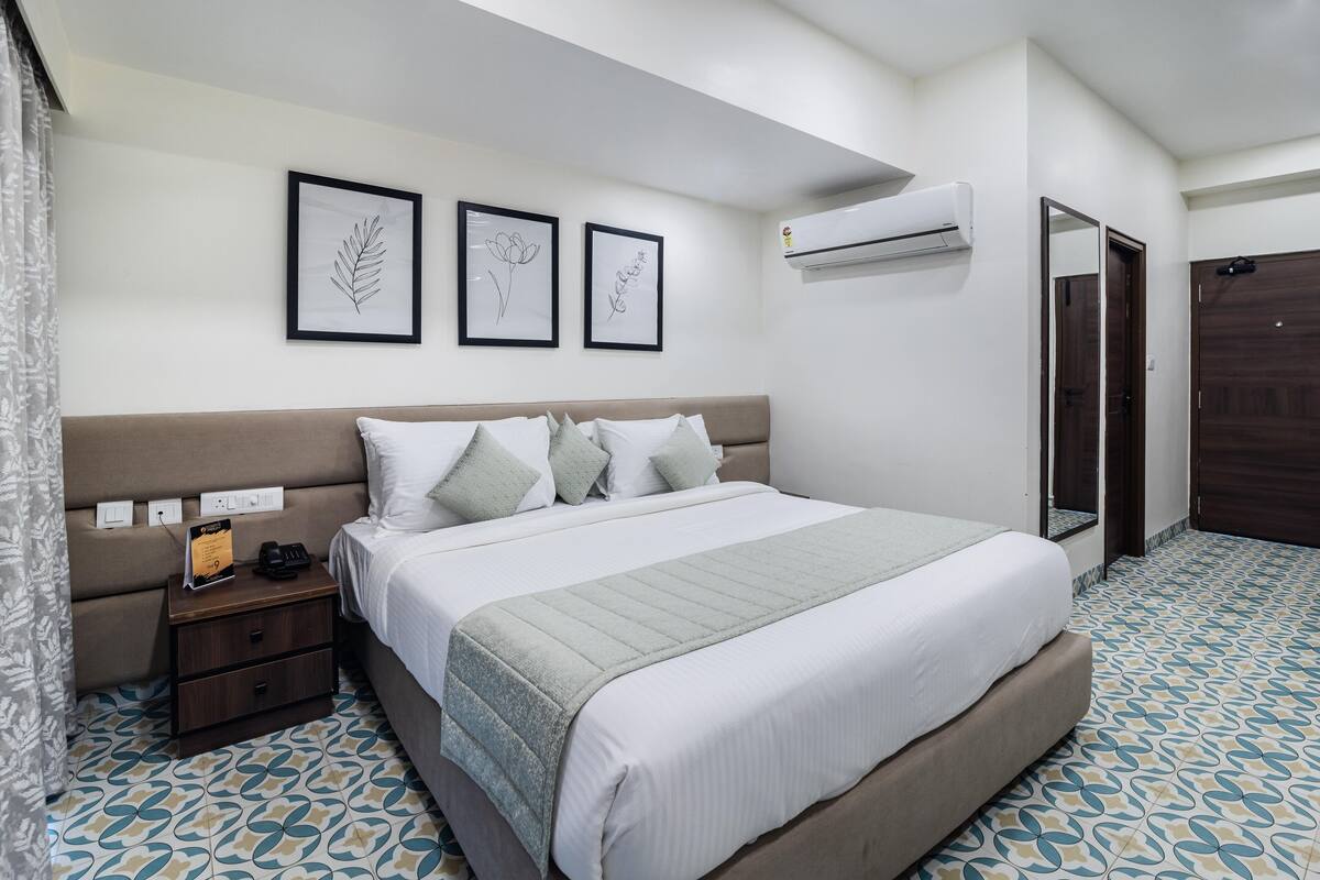 A neatly arranged bedroom with a bed, bedside tables, a nightstand, an air conditioning unit, and a door.