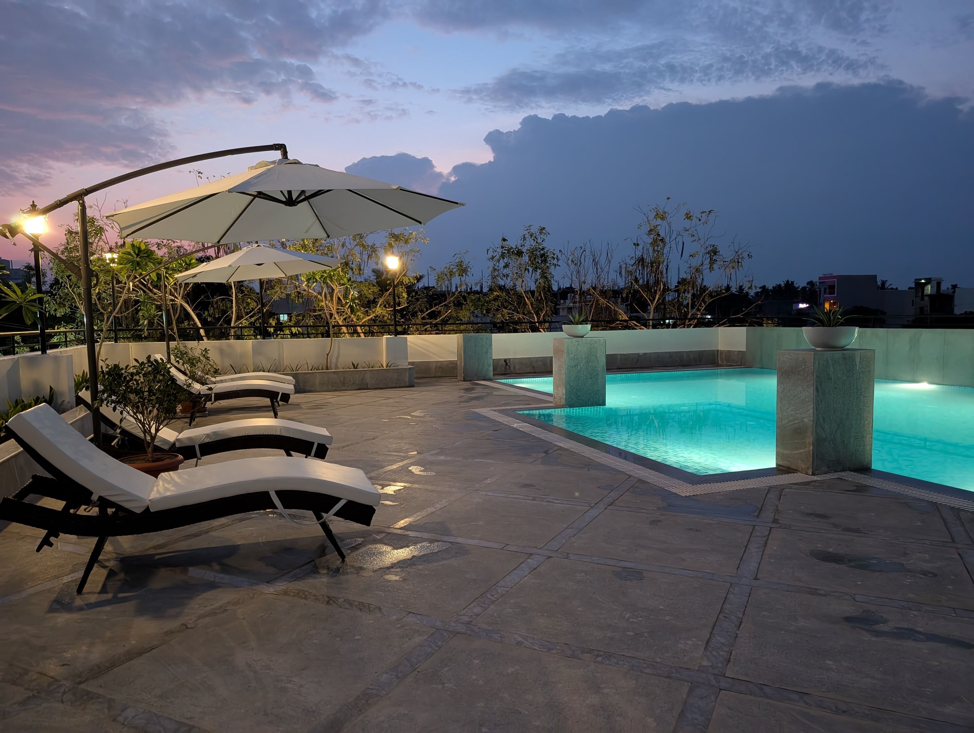 Un espace piscine aménagé sur le toit, avec des chaises longues et des parasols, entouré de plantes et bordé d’une piscine à eau claire.