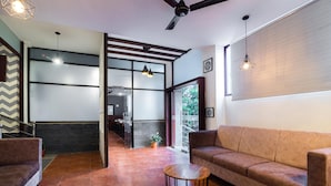 A modern interior with a sofa, a round wooden table, and pendant lighting. - Ashreya Suites Tiruvanamalai (Tiruvannamalai)