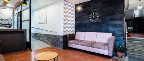A modern lobby with a sofa, a round wooden table, and a clock on the wall.