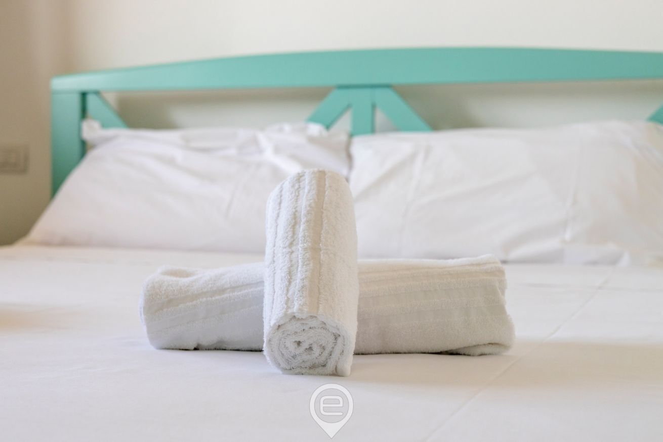 Un lit bien fait, avec du linge de lit blanc et une serviette enroulée placée au centre.