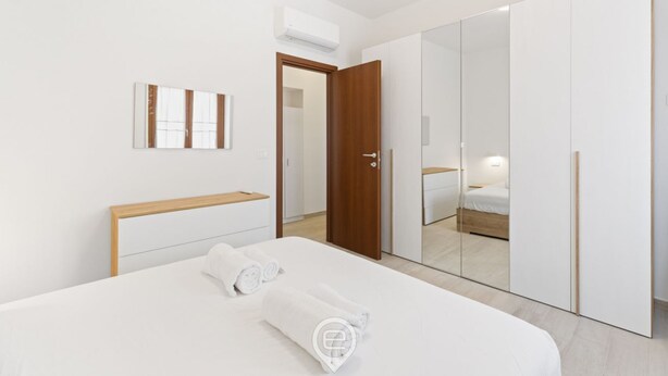 Une chambre d’hôtel moderne avec un grand lit, une tête de lit en bois, une armoire et un miroir.