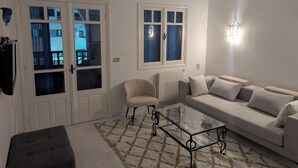 Un salon comprenant un canapé, un fauteuil, une table basse en verre et un tapis à motifs.
