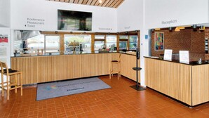 Een receptie met een houten balie, een receptiemedewerker en bewegwijzering naar de conferentiezaal, het restaurant en het toilet.