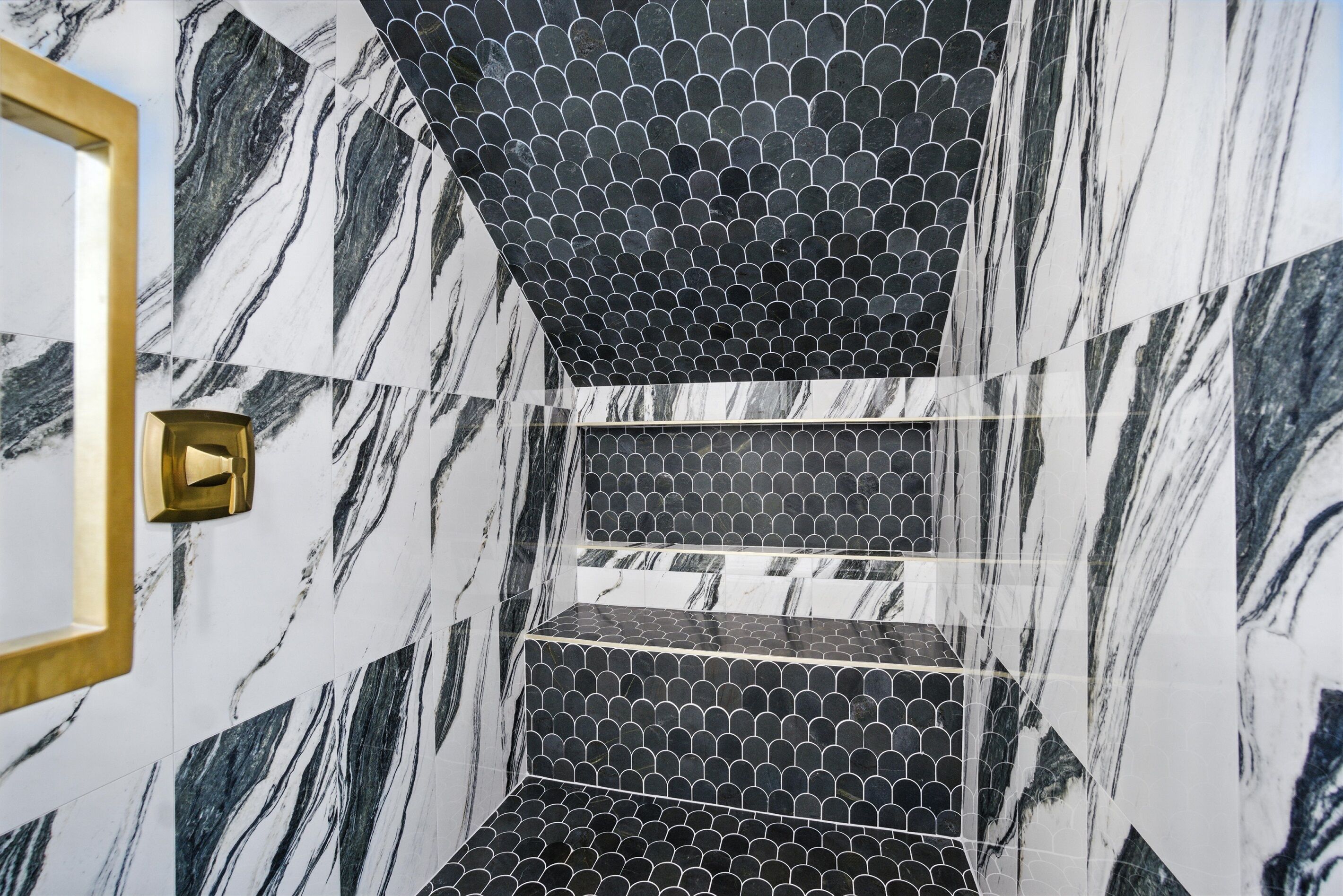 A bathroom with a marble wall, a gold-framed mirror, and a black and white tiled floor.