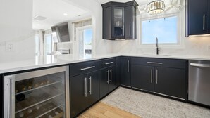 Una cocina moderna con armarios oscuros, lavavajillas de acero inoxidable y un refrigerador para vinos empotrado.
