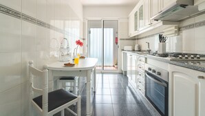 Una cucina stretta con mobili bianchi, un tavolo da pranzo con sedie, un fornello e una porta scorrevole in vetro che dà su un balcone.