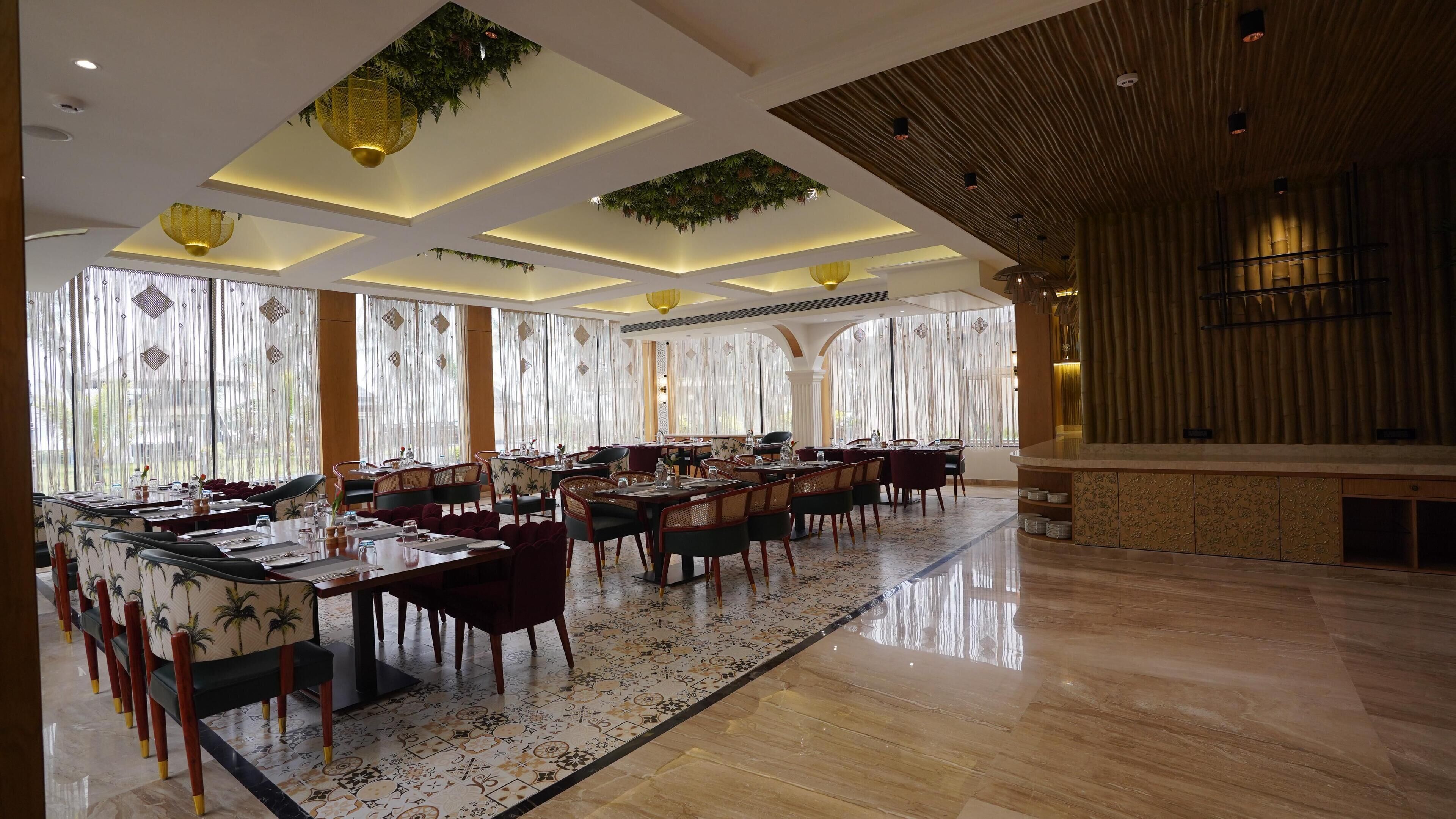 A spacious dining area with multiple tables and chairs, large windows with sheer curtains, and a polished floor.