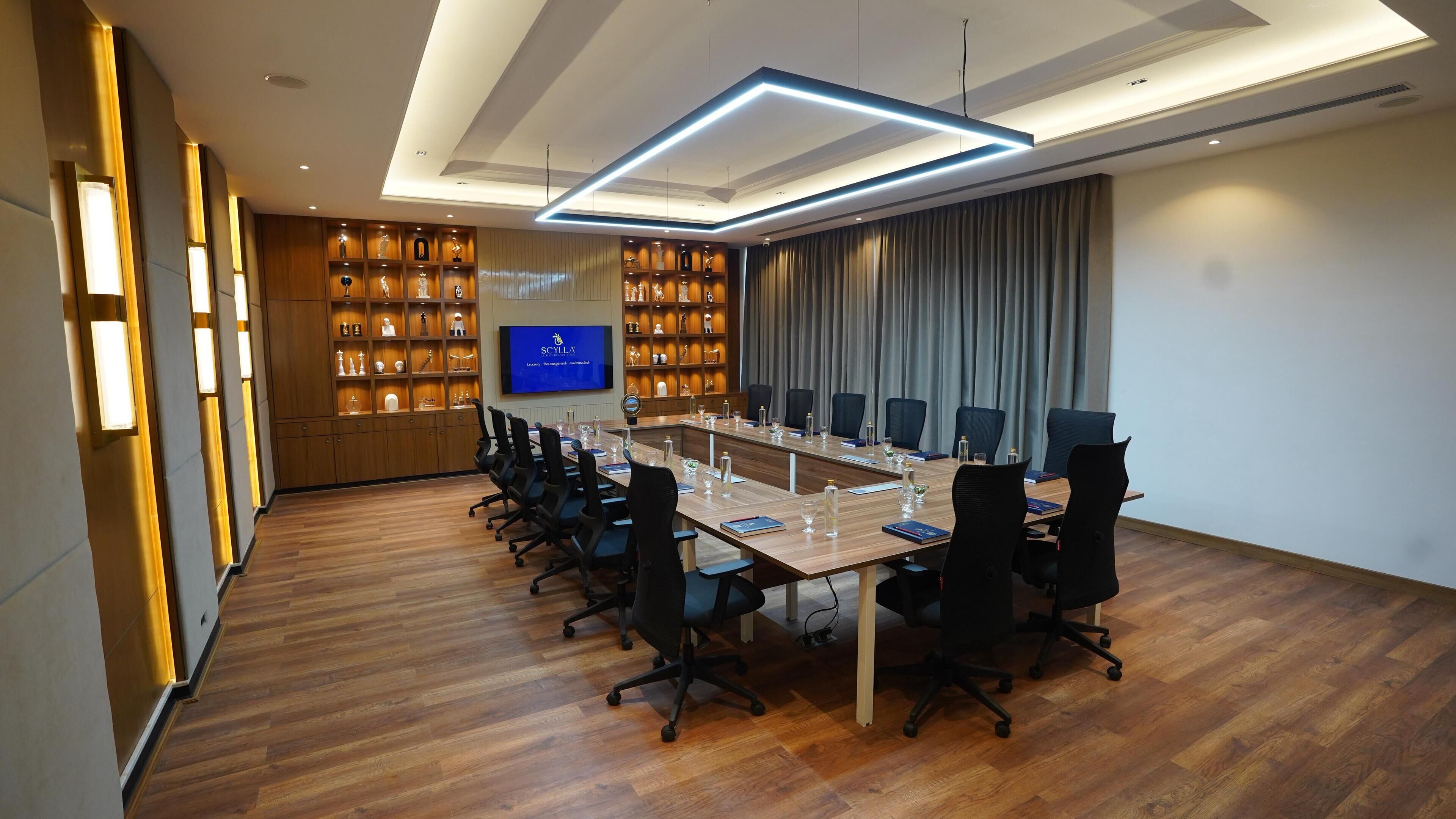 A conference room with a long table, black chairs, and a television screen displaying 'SCYLLA'.