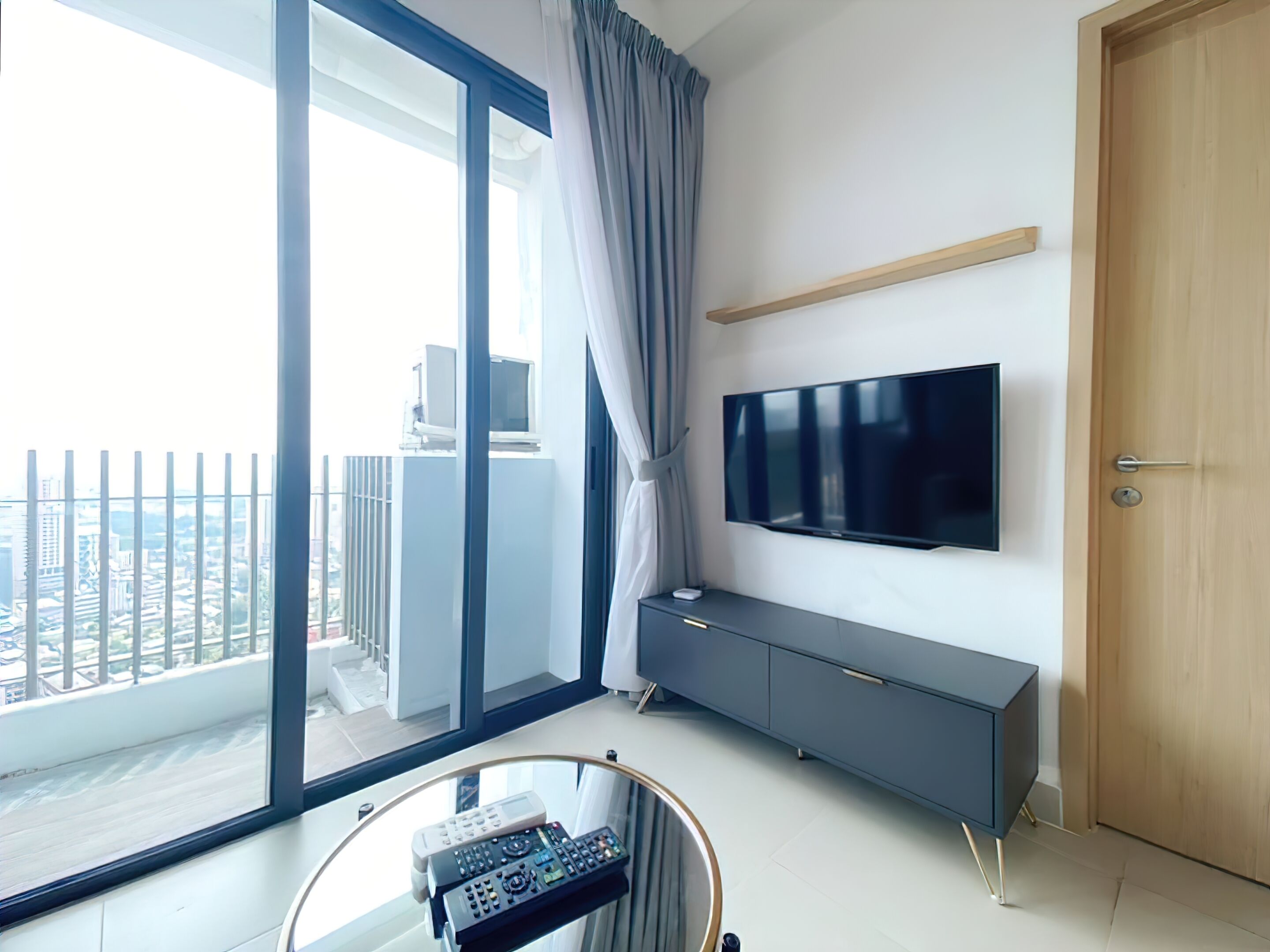 Una sala de estar moderna con un televisor grande, una mesa de centro de vidrio y un balcón con vista a la ciudad.