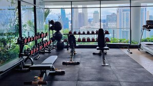 A modern gym with exercise equipment, large windows, and a view of a city skyline. - The Colony and the Luxe Infinity Pool (Kuala Lumpur)