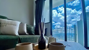 A hotel room with a balcony, a green sofa, two white cups on saucers, a black vase with reed sticks, and a white coffee maker. - The Colony and the Luxe Infinity Pool (Kuala Lumpur)
