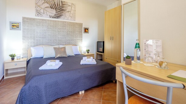 A bedroom with a bed, bedside tables, a desk, a mirror, and a wall with artwork. - Su Arghentu Country Hotel  (Laerru)