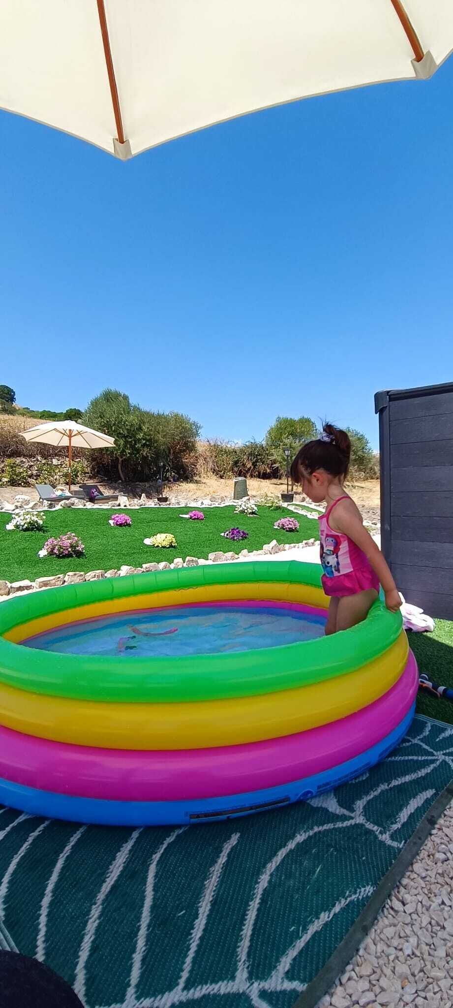 A child playing in a multi-colored inflatable pool on a patterned mat.