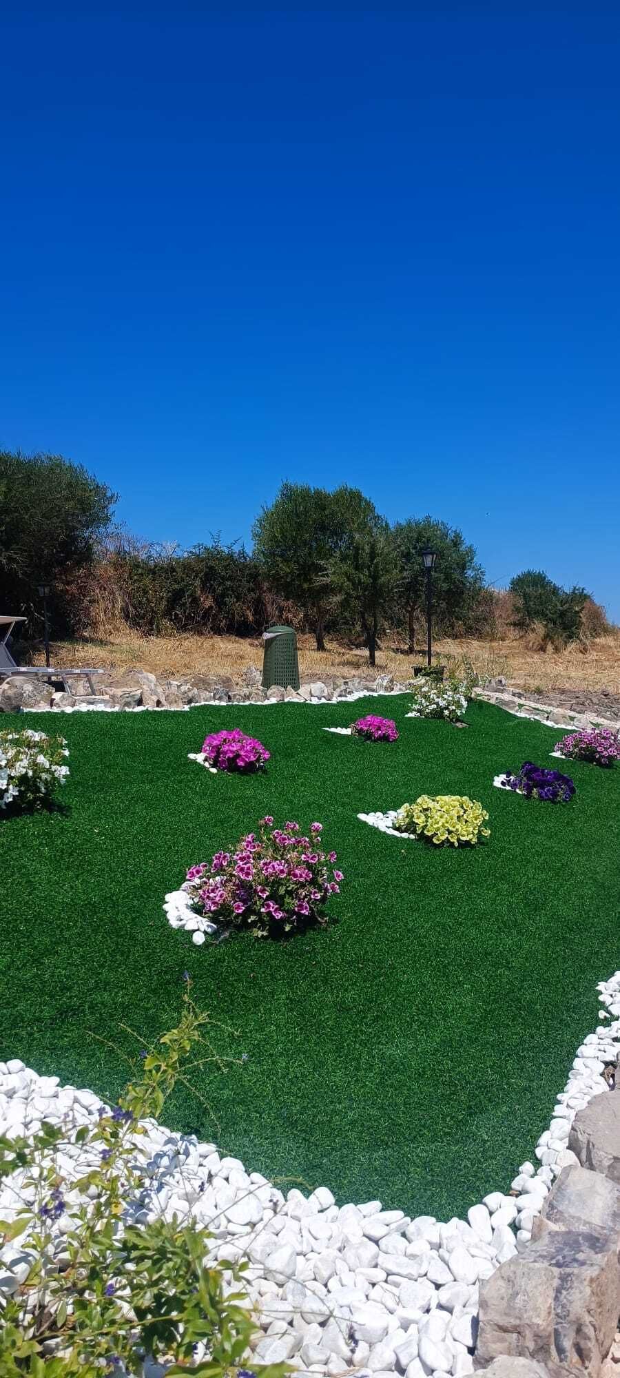Ein Garten mit Kunstgrasanlage, weißen Kiessteinen und unterschiedlichen Blumenarrangements.