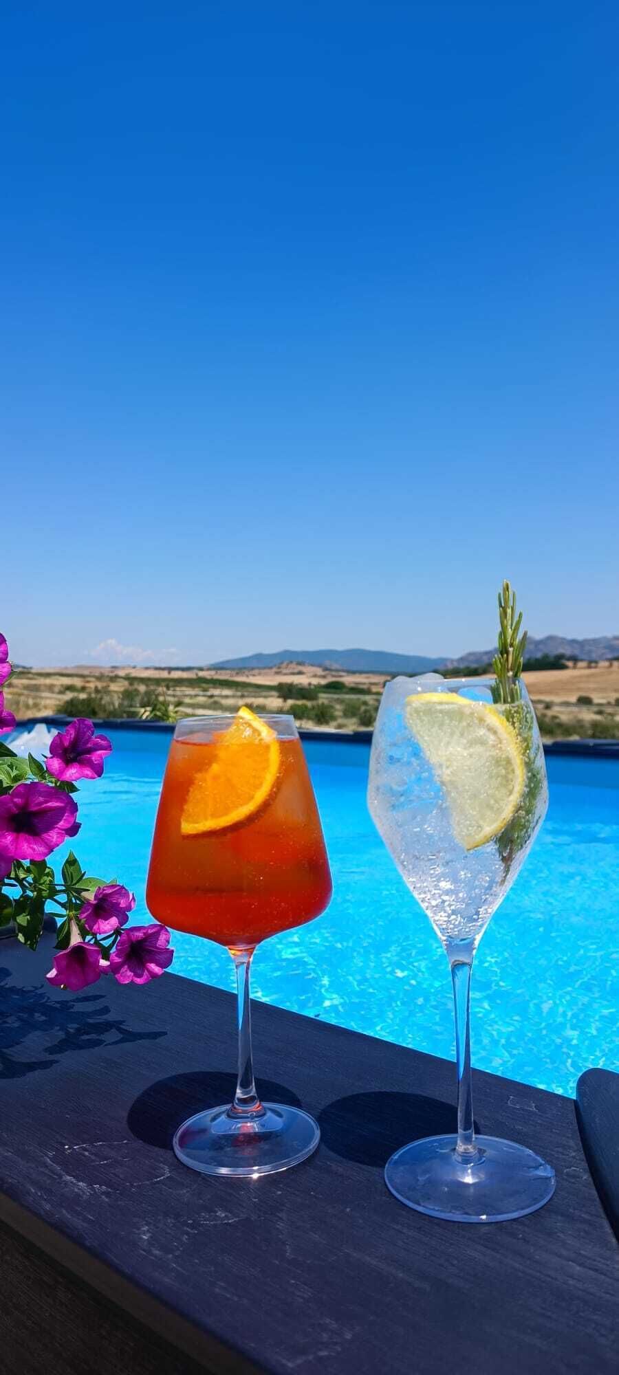 Zwei Cocktails auf einem Tisch neben einem Pool, im Hintergrund ein klarer, blauer Himmel.