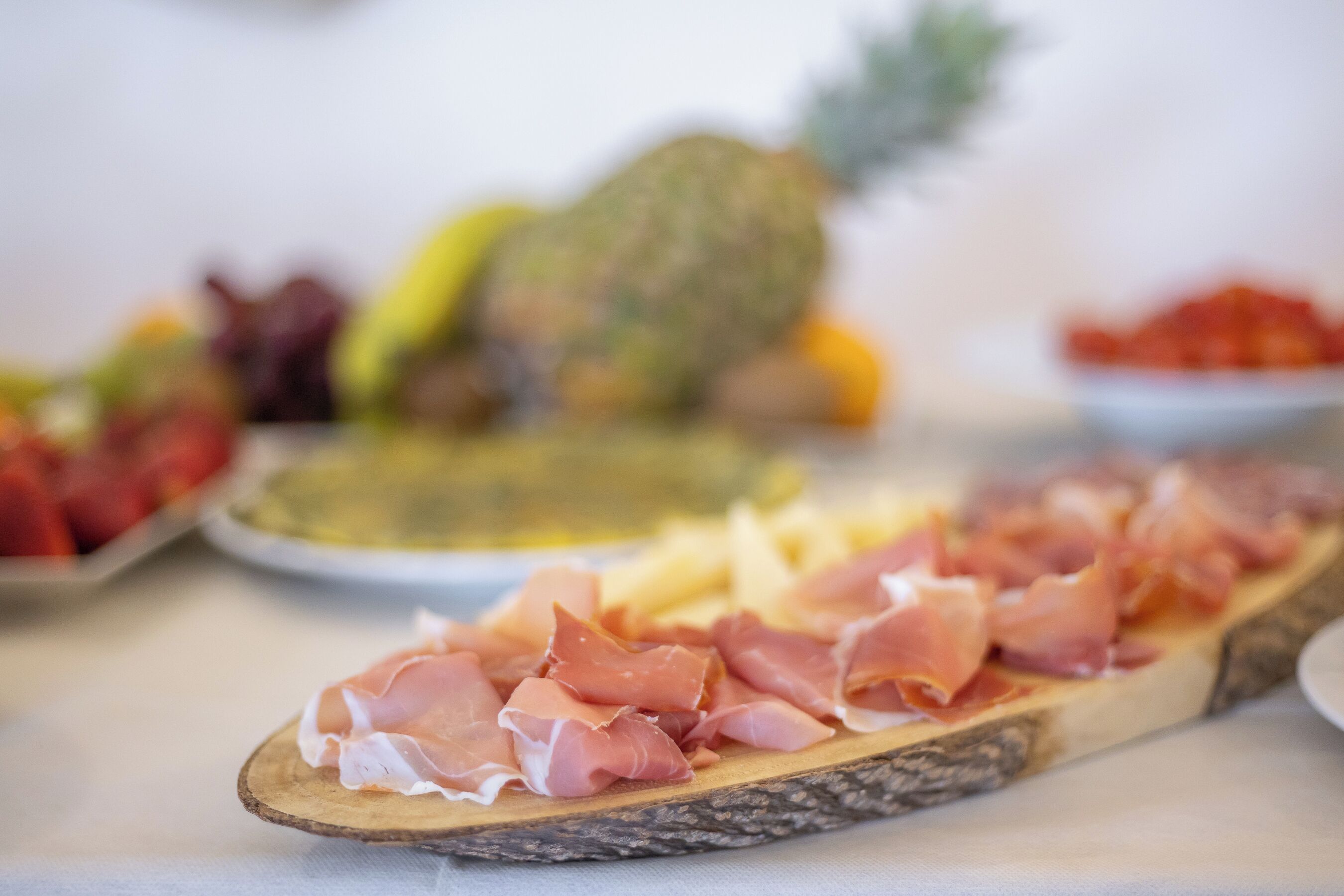 A wooden board with sliced prosciutto and a pineapple in the background.
