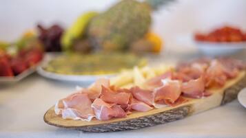 A wooden board with sliced prosciutto and a pineapple in the background.