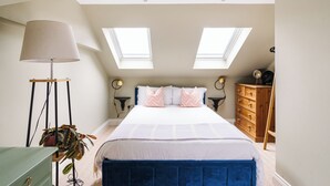 Un dormitorio con cama, tragaluces, lámpara, cómoda y planta.