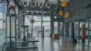 Une salle de sport offrant une vue sur la ville, dotée d’un plancher en bois et de divers équipements d’exercice.
