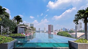 A rooftop infinity pool with lounge chairs and palm trees, overlooking a cityscape. - Opus Residences by Emily in Town (Kuala Lumpur)