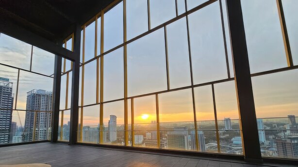 A spacious room with large windows offering a cityscape view at sunset. - Opus Residences by Emily in Town (Kuala Lumpur)