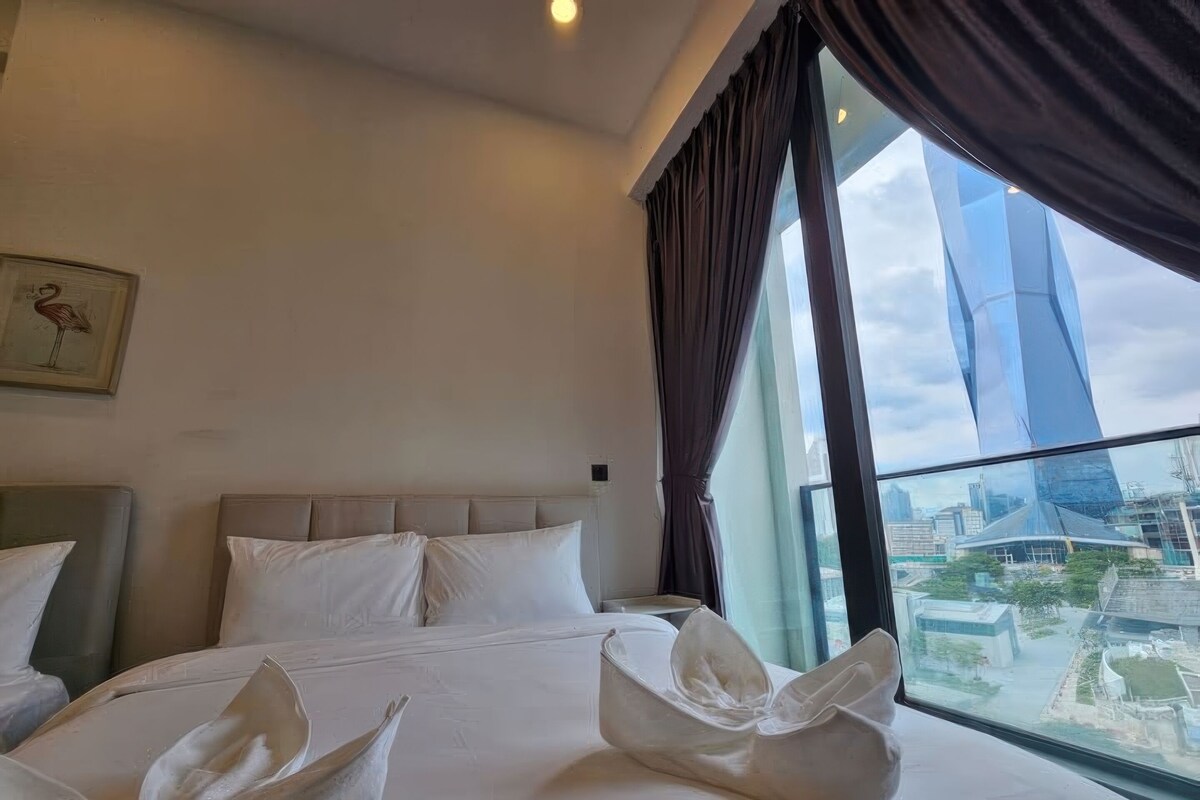 A hotel room with a large bed, a view of a modern building, and a framed picture on the wall.