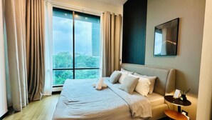 A modern hotel room with a large bed, a small side table, and a view of the cityscape through a large window. - Opus Residences by Emily in Town (Kuala Lumpur)