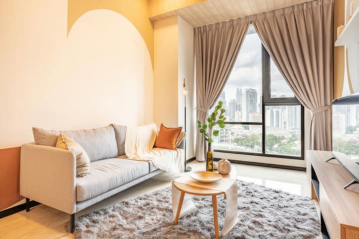 A modern living room with a sofa, a round coffee table, and a view of the city through large windows.