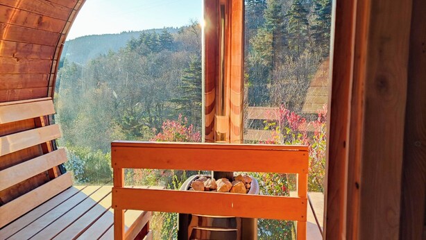 A wooden deck with a bench and a grill, overlooking a forested hillside.