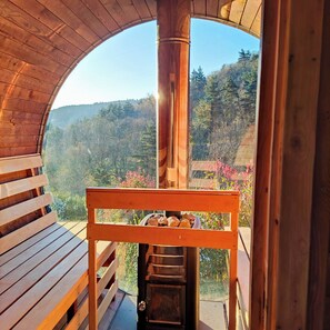 A wooden deck with a bench and a grill, overlooking a forested hillside.