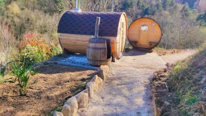 A rustic wooden barrel house with a chimney, a barrel-shaped door, and a small wooden barrel on a dirt path.