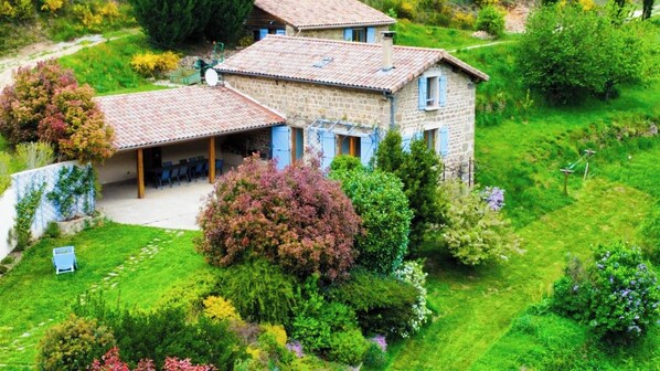A stone house with a tiled roof, surrounded by lush greenery and a well-maintained garden.
