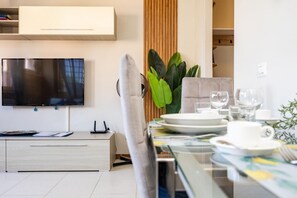 A modern dining area with a flat-screen TV, a dining table set with plates, glasses, and a plant.