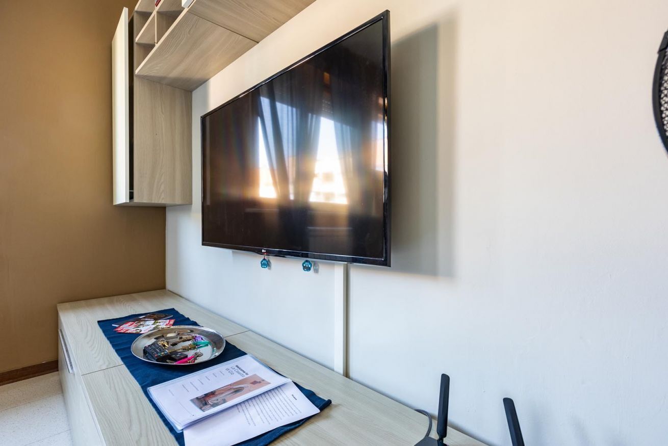 A room with a flat-screen TV mounted on the wall, a wooden table with a tray of items, and a small cabinet.