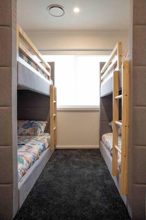 A narrow room with bunk beds, a window, and a carpeted floor.