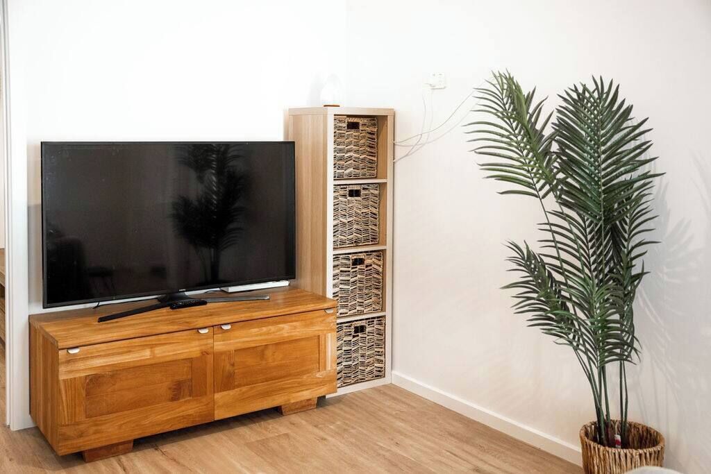 A living room with a wooden TV stand, a flat-screen TV, wicker baskets, and a tall potted plant.