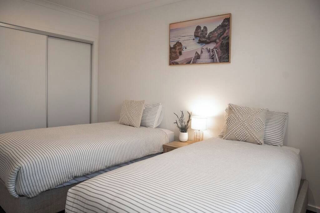 Et soveværelse med to senge, et natbord, en lampe og et billede på væggen.
