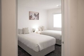 A bedroom with two beds, a window, and a wall-mounted picture. - Sandy Feet Retreat Su (Peterborough)