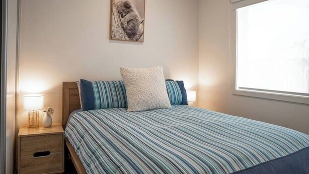 A bedroom with a bed, a nightstand, a lamp, and a framed picture on the wall. - Sandy Feet Retreat Su (Peterborough)